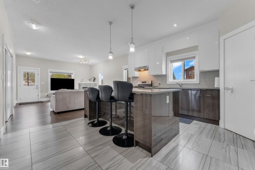 Bright kitchen featuring a central island with seating, pendant lighting, two-tone cabinetry, and a tile backsplash - 4506 49 Avenue, Beaumont, AB - Indoor Photo Showing Kitchen With Upgraded Kitchen