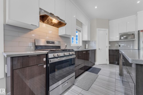 Modern kitchen featuring two-tone cabinetry with white upper cabinets and dark wood-finish lower cabinets, stainless steel appliances, a subway tile backsplash, light-toned countertops, and large format floor tiling - 4506 49 Avenue, Beaumont, AB - Indoor Photo Showing Kitchen With Upgraded Kitchen