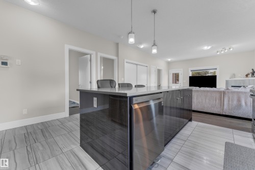 Expansive kitchen island featuring a smooth countertop, integrated stainless steel dishwasher, and dark wood-finish cabinetry - 4506 49 Avenue, Beaumont, AB - Indoor Photo Showing Kitchen