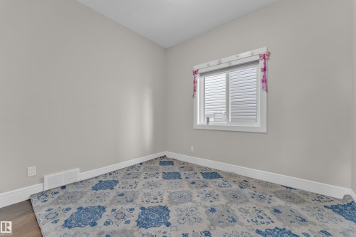 Neutral-toned interior room featuring a large window with horizontal blinds, white trim, wood-finish flooring, and a patterned area rug - 4506 49 Avenue, Beaumont, AB - Indoor Photo Showing Other Room