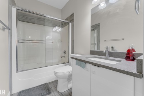 Bathroom featuring a tub/shower combination with sliding glass doors, a vanity with an integrated sink, and a gray countertop - 4506 49 Avenue, Beaumont, AB - Indoor Photo Showing Bathroom