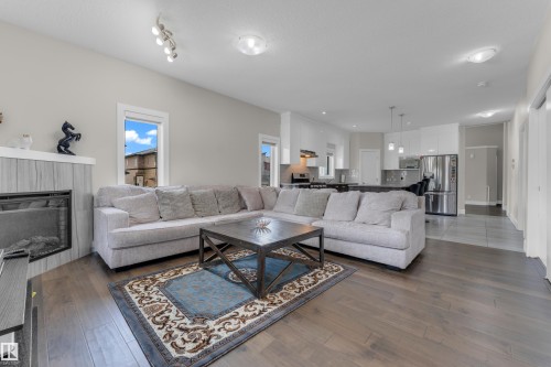 Expansive open-concept living space featuring wood-finish flooring, a corner fireplace with a tiled surround, and multiple windows - 4506 49 Avenue, Beaumont, AB - Indoor Photo Showing Living Room With Fireplace