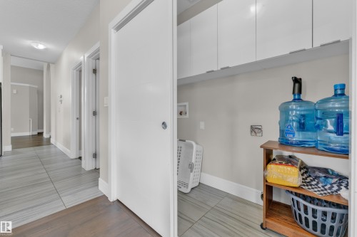 Dedicated laundry area featuring white upper cabinetry, light gray wall paint, and gray wood-finish tile flooring - 4506 49 Avenue, Beaumont, AB - Indoor Photo Showing Other Room