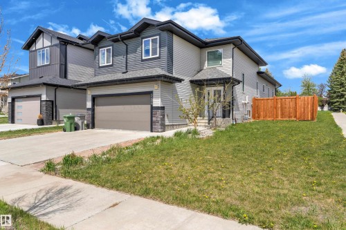 Contemporary residential exterior featuring a two-car garage, grey siding, stone accents, a covered entry, and a wood privacy fence - 4506 49 Avenue, Beaumont, AB - Outdoor With Facade