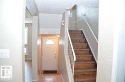 Entryway featuring wood-finish flooring, a white door with an arched window insert, and a staircase with wood-finish treads and white railings - 