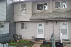 Duplex exterior featuring light gray horizontal siding, white-framed windows, and two distinct entrances with white storm doors - 