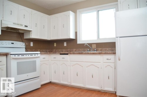 Kitchen featuring white cabinetry, wood-finish flooring, a white electric range, a white refrigerator, and a double-basin sink - 14210 31 Street Nw, Edmonton, AB - Indoor Photo Showing Kitchen