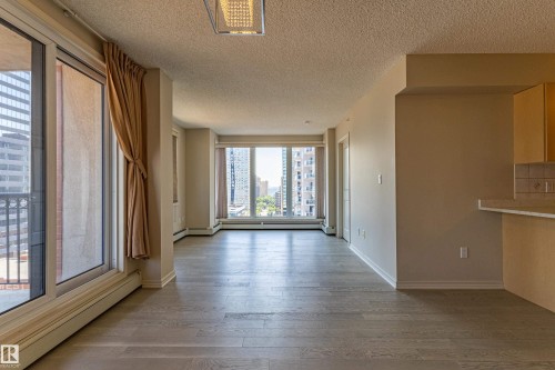 Bright living area featuring expansive windows, wood-finish flooring, neutral wall tones, and a built-in breakfast bar with tiled backsplash - #1501 10180 104 St Nw, Edmonton, AB - Indoor Photo Showing Other Room