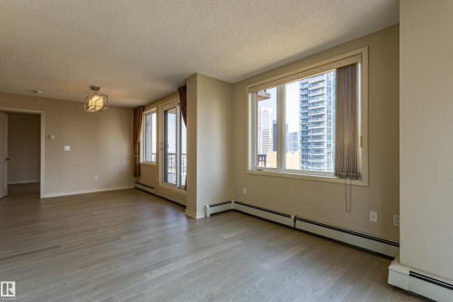 Spacious interior featuring wood-finish flooring, a contemporary ceiling light fixture, a balcony access door, and a large window with vertical blinds - #1501 10180 104 St Nw, Edmonton, AB - Indoor Photo Showing Other Room