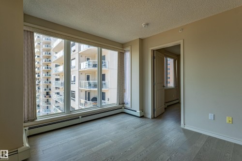 Expansive window wall with vertical blinds, light wood-finish flooring, neutral paint palette, baseboard heating, and ceiling-mounted smoke detector - #1501 10180 104 St Nw, Edmonton, AB - Indoor Photo Showing Other Room