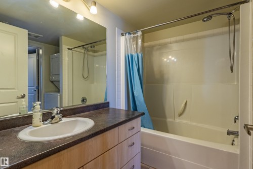 Bathroom featuring a vanity with an integrated sink, dark countertop, and wood-finish cabinetry - #1501 10180 104 St Nw, Edmonton, AB - Indoor Photo Showing Bathroom