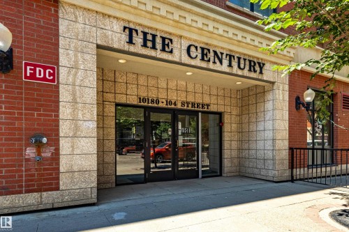Building entrance featuring a prominent "THE CENTURY" sign, stone tile facade, and red brick accents - #1501 10180 104 St Nw, Edmonton, AB - Outdoor With Exterior