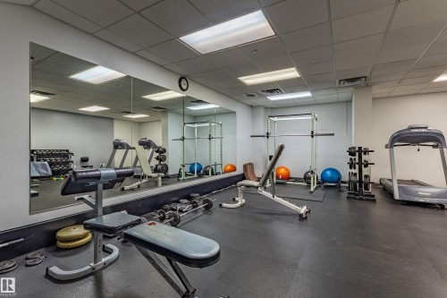 Dedicated fitness area featuring rubber flooring, extensive wall-mounted mirrors, recessed lighting, and a drop ceiling - #1501 10180 104 St Nw, Edmonton, AB - Indoor Photo Showing Gym Room