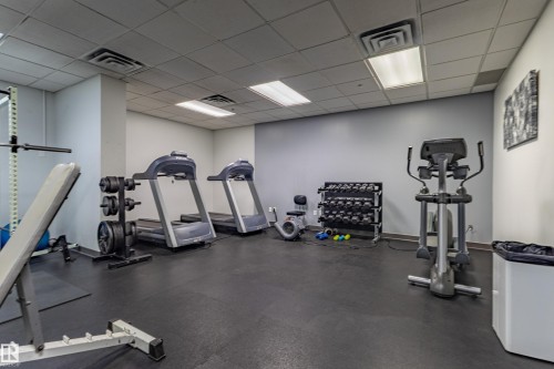 Dedicated fitness space featuring a rubber flooring system, suspended ceiling with integrated lighting, and neutral wall tones - #1501 10180 104 St Nw, Edmonton, AB - Indoor Photo Showing Gym Room