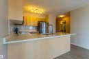 Kitchen featuring a breakfast bar with stone-finish countertops, stainless steel appliances, wood-finish cabinetry, ceramic tile backsplash, and a modern gooseneck faucet - #1501 10180 104 St Nw, Edmonton, AB  - Indoor Photo Showing Kitchen 