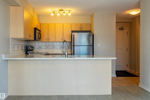 Kitchen featuring light wood-finish cabinetry, stainless steel appliances, a white countertop island, and a decorative tile backsplash - #1501 10180 104 St Nw, Edmonton, AB - Indoor Photo Showing Kitchen