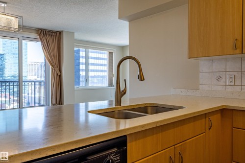 Kitchen featuring light wood cabinetry, light-toned countertops, and a double basin sink with a bronze-finish faucet - #1501 10180 104 St Nw, Edmonton, AB - Indoor Photo Showing Kitchen With Double Sink
