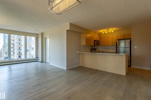 Open-concept living space featuring wood-finish flooring, a full wall of windows, and a modern rectangular chandelier - #1501 10180 104 St Nw, Edmonton, AB - Indoor Photo Showing Kitchen
