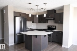 Modern kitchen featuring dark wood-finish cabinetry, stainless steel appliances, a white subway tile backsplash, and a hexagonal island with a light-colored countertop - 