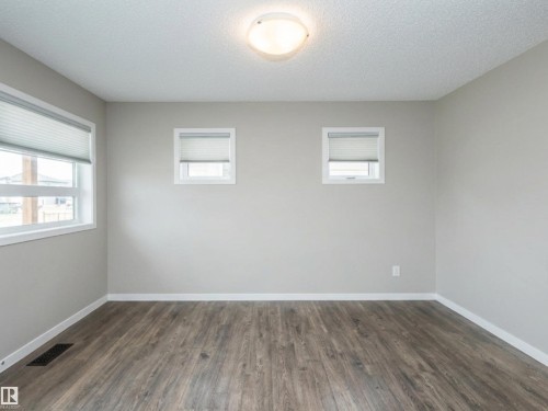 Neutral-toned living room featuring wood-finish flooring, white baseboards, and light gray walls - 17263 9 Avenue Sw, Edmonton, AB 