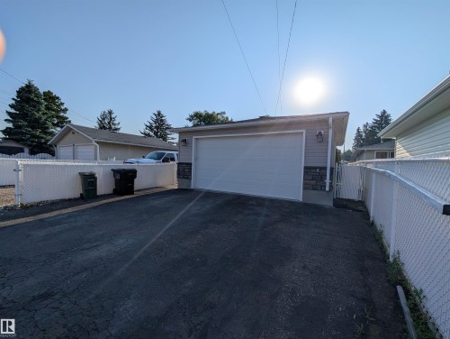 Detached garage featuring a white overhead door, horizontal siding, and stone veneer accents - 13216 117 Street Nw, Edmonton, AB - Outdoor