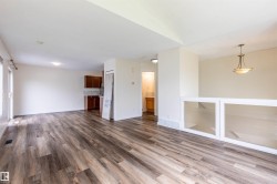 Spacious room featuring wood-finish flooring, a contemporary ceiling light fixture, white walls, and a glass-paneled railing - 