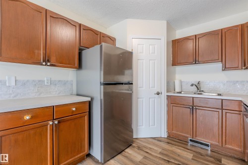 Kitchen featuring wood-finish cabinetry with silver hardware, light countertops, and a subway tile backsplash - #D 10102 103 St, Morinville, AB - Indoor Photo Showing Kitchen With Double Sink