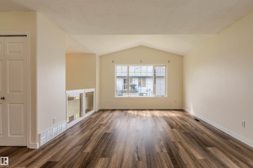Spacious room featuring vaulted ceilings, wood-finish flooring, a large multi-pane window, and neutral wall tones - #D 10102 103 St, Morinville, AB - Indoor