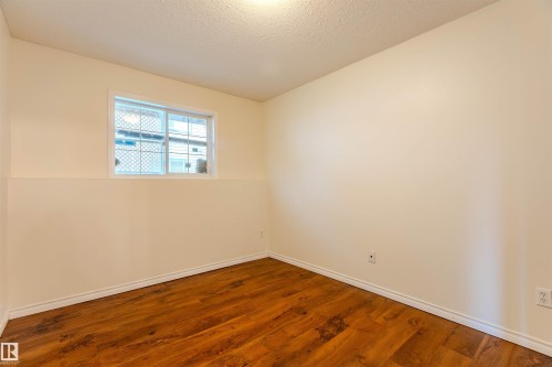 Room featuring wood-finish flooring, white baseboards, a white-framed window, neutral painted walls, and a textured ceiling - #D 10102 103 St, Morinville, AB - Indoor Photo Showing Other Room