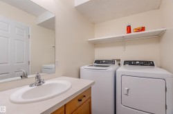 Laundry area featuring a built-in sink with countertop, wood-finish cabinetry, a wall-mounted mirror, and overhead shelving - 
