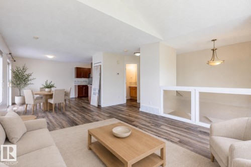 Open-concept living area featuring wood-finish flooring, a contemporary chandelier, white wall finishes, and a functional half-wall with built-in display niches - #D 10102 103 St, Morinville, AB - Indoor Photo Showing Living Room