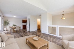 Open-concept living area featuring wood-finish flooring, a contemporary chandelier, white wall finishes, and a functional half-wall with built-in display niches - 