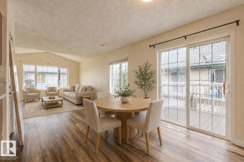Open-concept living area featuring wood-finish flooring, vaulted ceilings, and extensive natural light from multiple windows and a glass sliding door - #D 10102 103 St, Morinville, AB - Indoor Photo Showing Dining Room