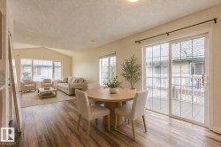 Open-concept living area featuring wood-finish flooring, vaulted ceilings, and extensive natural light from multiple windows and a glass sliding door - 