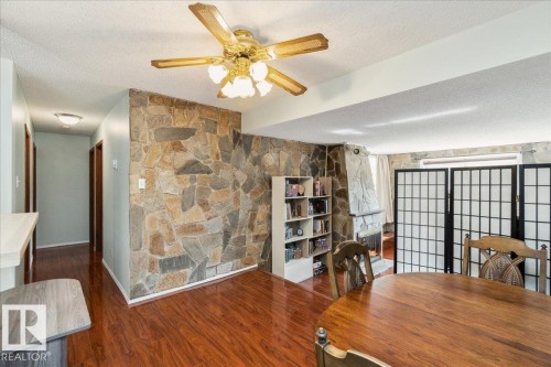 Interior featuring wood-finish flooring, a stone-accent wall, and a stone fireplace - #112 2904 139 Av Nw, Edmonton, AB - Indoor Photo Showing Dining Room