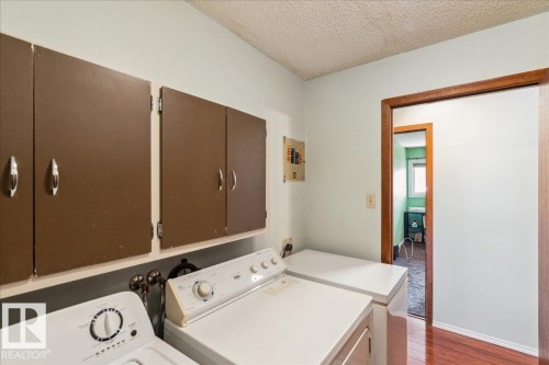 Dedicated laundry area featuring overhead cabinetry, wood-finish flooring, and a solid wood door frame - #112 2904 139 Av Nw, Edmonton, AB - Indoor Photo Showing Laundry Room