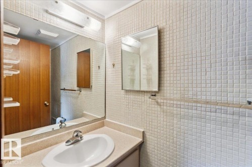 Bathroom vanity with an integrated sink and chrome faucet, set against a tiled wall - #112 2904 139 Av Nw, Edmonton, AB - Indoor Photo Showing Bathroom