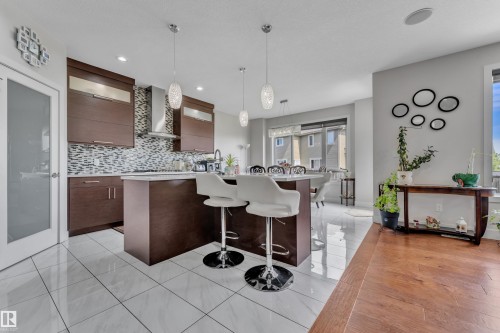 Contemporary kitchen featuring dark wood-finish cabinetry, a patterned tile backsplash, and a central island with a white countertop - 3001 55 Street, Beaumont, AB - Indoor