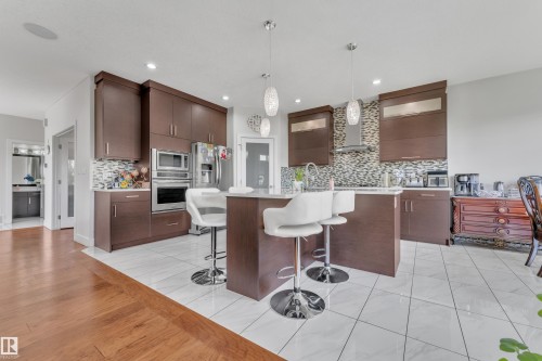 Kitchen featuring dark wood-finish cabinetry, stainless steel appliances, a center island with pendant lighting, and a mosaic tile backsplash - 3001 55 Street, Beaumont, AB - Indoor Photo Showing Kitchen With Upgraded Kitchen