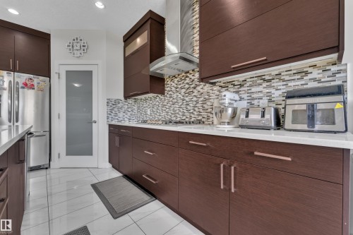 Modern kitchen featuring dark wood-finish cabinetry with linear pulls, white countertops, and a mosaic tile backsplash - 3001 55 Street, Beaumont, AB - Indoor Photo Showing Kitchen With Upgraded Kitchen