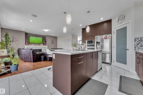 Contemporary kitchen island featuring a light-toned countertop, dark wood-finish cabinetry, and three decorative pendant lights - 3001 55 Street, Beaumont, AB - Indoor Photo Showing Kitchen With Upgraded Kitchen