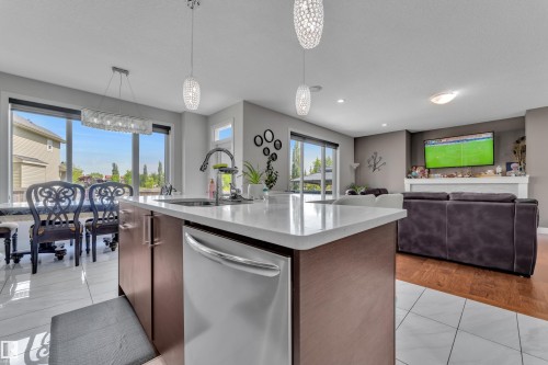 Kitchen island with a white solid surface countertop and undermount sink, stainless steel dishwasher, and two pendant light fixtures - 3001 55 Street, Beaumont, AB - Indoor