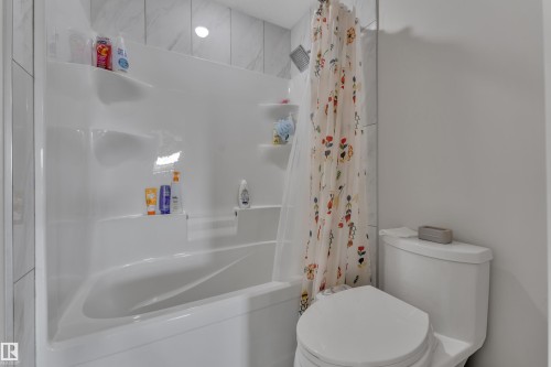 White integrated tub and shower unit featuring built-in shelving, a rainfall showerhead, and a white toilet - 3001 55 Street, Beaumont, AB - Indoor Photo Showing Bathroom
