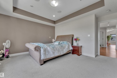 Recessed lighting illuminates this carpeted room featuring a tray ceiling, two-tone walls, and a doorway leading to a hallway with wood-finish flooring - 3001 55 Street, Beaumont, AB - Indoor Photo Showing Bedroom