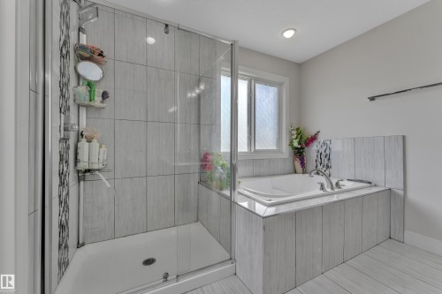 Modern bathroom featuring a glass-enclosed shower with tile surround, a built-in soaking tub with a tiled facade, a window, recessed lighting, and a towel bar - 3001 55 Street, Beaumont, AB - Indoor Photo Showing Bathroom