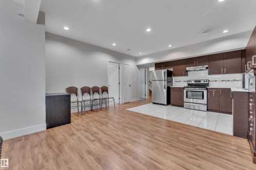 Open-concept living space featuring wood-finish flooring, a contemporary kitchen with stainless steel appliances, recessed lighting, and white tile flooring in the kitchen area - 3001 55 Street, Beaumont, AB - Indoor Photo Showing Kitchen