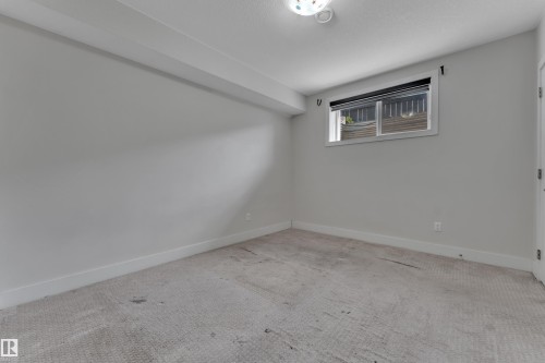 Neutral-toned room featuring a single window with a black roller shade, light gray walls, white baseboards, and a textured carpeted floor - 3001 55 Street, Beaumont, AB - Indoor Photo Showing Other Room