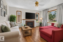 Living area featuring wood-finish flooring, a fireplace with a tiled surround, a large window, a ceiling fan, and crown molding - 