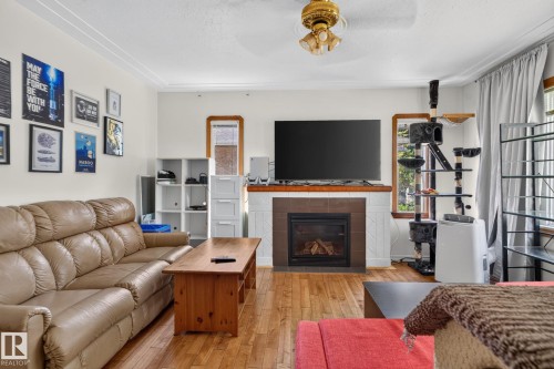 Living area featuring wood-finish flooring, a fireplace with a tiled surround, and white crown molding - 12229 88 Street Nw, Edmonton, AB - Indoor Photo Showing Living Room With Fireplace