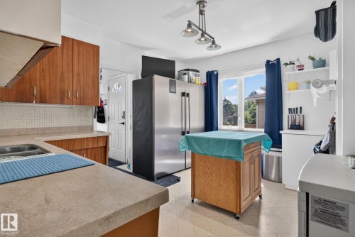 Kitchen featuring wood-finish cabinetry, solid surface countertops, a mosaic tile backsplash, and an overhead light fixture - 12229 88 Street Nw, Edmonton, AB - Indoor Photo Showing Kitchen With Double Sink